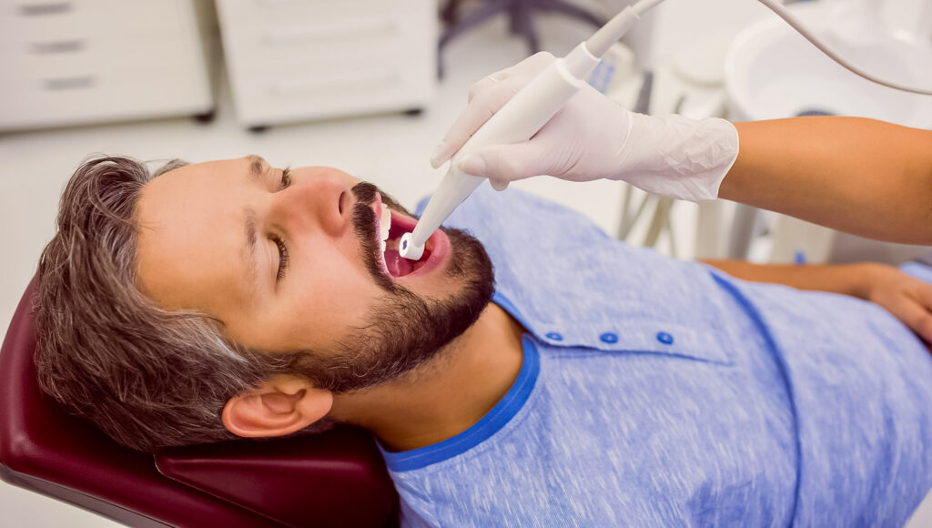 Homem de camisa azul sendo atendido por dentista.