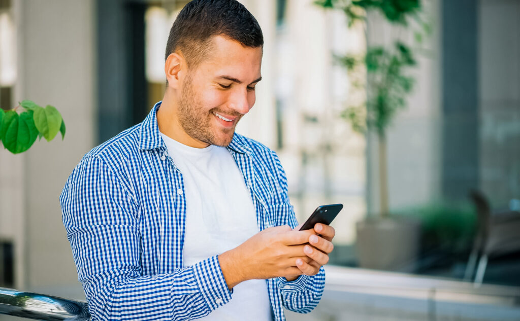 Homem sorrindo mexendo no celular.