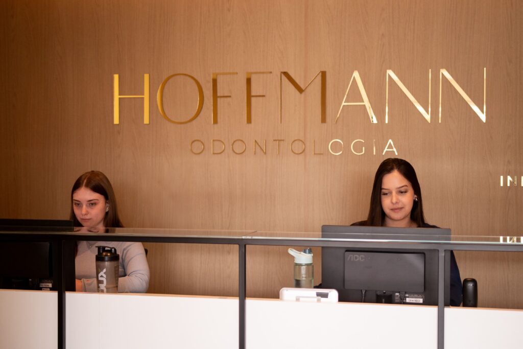 Recepcionistas da Hoffmann odontologia mexendo no ssitema clinicorp atrás do balcão.